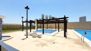 A rooftop pool area with a pergola, lounge chairs, and a view of city buildings. - Bloomfields STU with Canal View Julphar Al Reem (Abu Dabi)