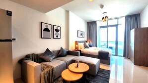 A modern hotel room with a sofa, a bed, a small wooden table, and a balcony with a view. - Bloomfields STU with Canal View Julphar Al Reem (Abu Dabi)