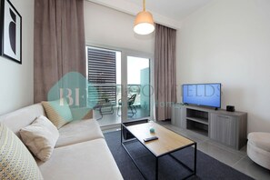 A modern living room with a sofa, coffee table, TV, and sliding glass doors leading to a balcony. - Bloomfields STU with Balcony Leonardo (Abu Dabi)