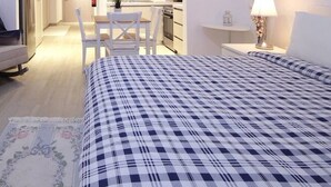 Ein Hotelzimmer mit kariertem Bettbezug, einem weißen Schreibtisch, einem Stuhl und einem kleinen Tisch mit einer Lampe.