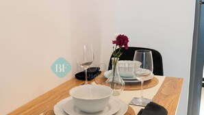 Een eettafel gedekt met een witte kom, twee wijnglazen en een vaas met bloemen.