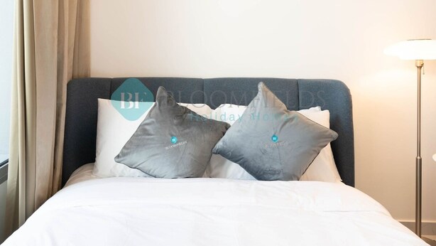 A hotel room with a bed, two pillows, a lamp, and a window with curtains. - Bloomfields Elegant STU in Oasis Masdar City (Abu Dabi)
