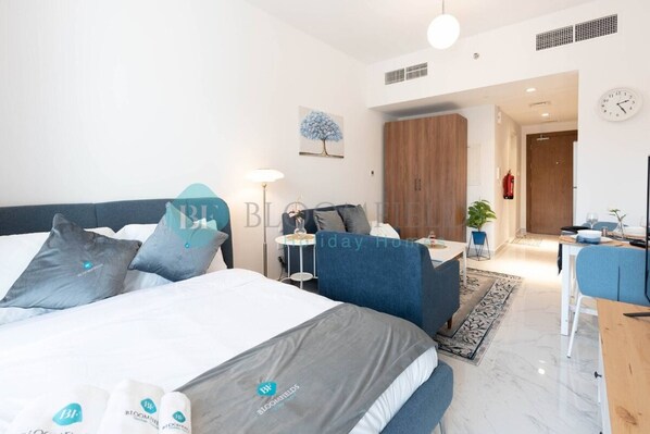 Een moderne hotelkamer met een groot bed, een bureau en een stoel. Er hangt een klok aan de muur en er staat een plant in de hoek.