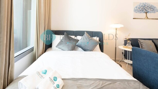 Una habitación de hotel con una cama, almohadas, una mesita de noche, una lámpara y un cuadro en la pared.