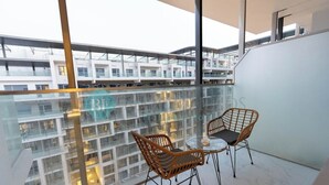 Un balcon avec deux fauteuils en osier et une table en verre, donnant sur un immeuble moderne à étages multiples et doté de balcons.