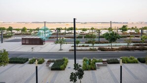 Amplia zona urbana con un sendero pavimentado, vegetación y una vista distante de un terreno llano.