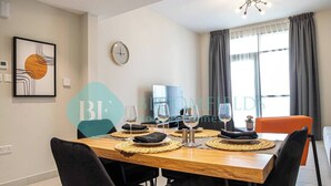 A dining area with a wooden table set for four, surrounded by black chairs. A clock and a framed artwork are on the wall. - Bloomfields Stylish 1BR in Reflections Al Reem (Abu Dabi)
