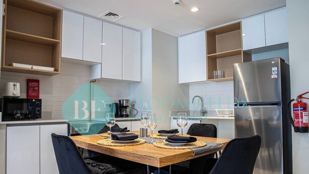 A modern kitchen with white cabinets, a stainless steel refrigerator, and a dining table set for four. - Bloomfields Stylish 1BR in Reflections Al Reem (Abu Dabi)