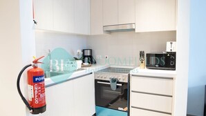 A kitchen with white cabinets, a black and blue oven, a microwave, and a fire extinguisher. - Bloomfields Stylish STU in Waters Edge Yas Island (Abu Dabi)