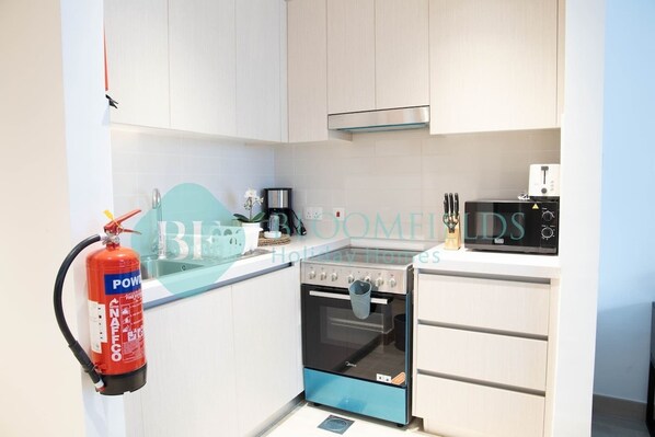 A kitchen with white cabinets, a black and blue oven, a microwave, and a fire extinguisher. - Bloomfields Stylish STU in Waters Edge Yas Island (Abu Dabi)