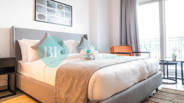 A modern bedroom with a large bed, a framed artwork above the bed, a grey headboard, and a view of the outside balcony. - Bloomfields Stylish STU in Waters Edge Yas Island (Abu Dabi)