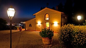A small building with a single entrance, a visible window, and a door, surrounded by a gravel path and potted plants. - Cottage - The Hill Below - Imagine a place just for you (Toscana)
