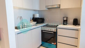 Eine moderne Küche mit hellen Holzschränken, einer Edelstahl-Dunstabzugshaube, einer schwarzen Mikrowelle, einer Kaffeemaschine und einem blauen Backofen.