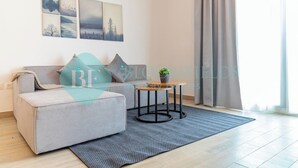A modern living room with a grey sofa, a small round table with a plant, and a grey rug. There are four framed pictures on the wall above the sofa. - Bloomfields Modern 1BR in Waters Edge Yas Island (Abu Dabi)