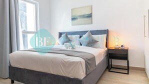 A modern bedroom with a large bed, a bedside table with a lamp, a window with curtains, and a wall-mounted artwork. - Bloomfields Modern 1BR in Waters Edge Yas Island (Abu Dabi)