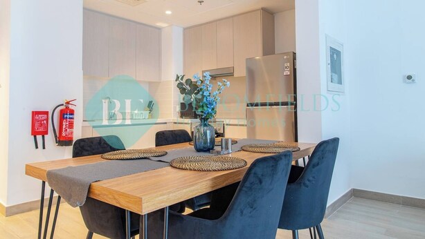 A modern kitchen with light wood cabinets, a stainless steel refrigerator, and a vase with blue flowers on the island. - Bloomfields Modern 1BR in Waters Edge Yas Island (Abu Dabi)