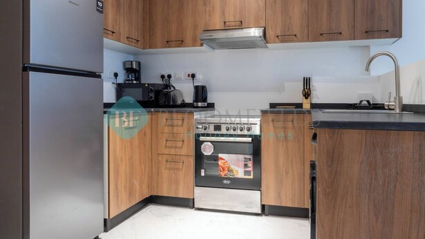 A modern kitchen with wooden cabinets, a stainless steel refrigerator, a built-in oven, and a coffee maker. - Bloomfields Mesmerizing 1BR in Oasis Masdar City (Abu Dabi)