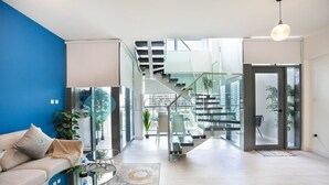A modern living room with a blue accent wall, a glass staircase, and a view of the city.