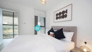 A modern bedroom with a large bed, a bedside table with a lamp, and a framed artwork on the wall.