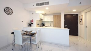 A modern kitchen with white cabinets, a central island, and a dining area with white chairs.