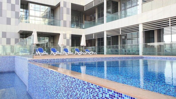 A modern hotel with a large indoor swimming pool, multiple balconies, and lounge chairs.