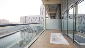 A modern balcony with a glass railing overlooking a water body and a cityscape.