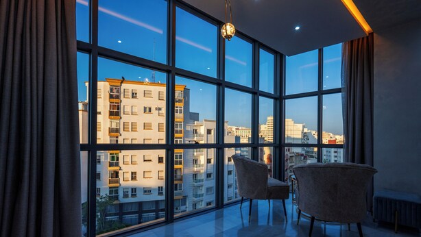 Una habitación moderna con ventanas amplias, dos sillas y una lámpara colgante.