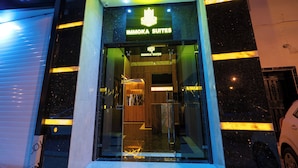 El exterior de ImmoKa Suites, con acceso de vidrio y señalización iluminada.
