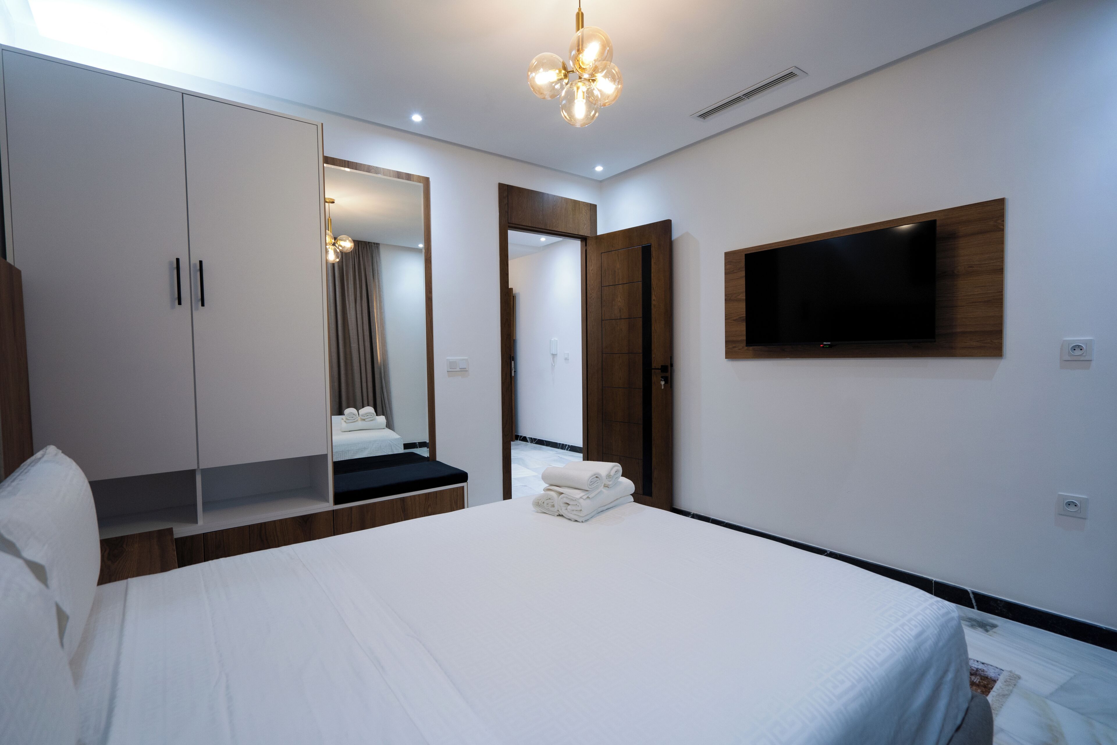 Une chambre d’hôtel moderne avec un grand lit, une armoire, un téléviseur fixé au mur et un miroir qui reflète la pièce.