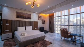 Een moderne hotelkamer met een groot bed, een zithoek met een tafel, en grote ramen met uitzicht op de stad.