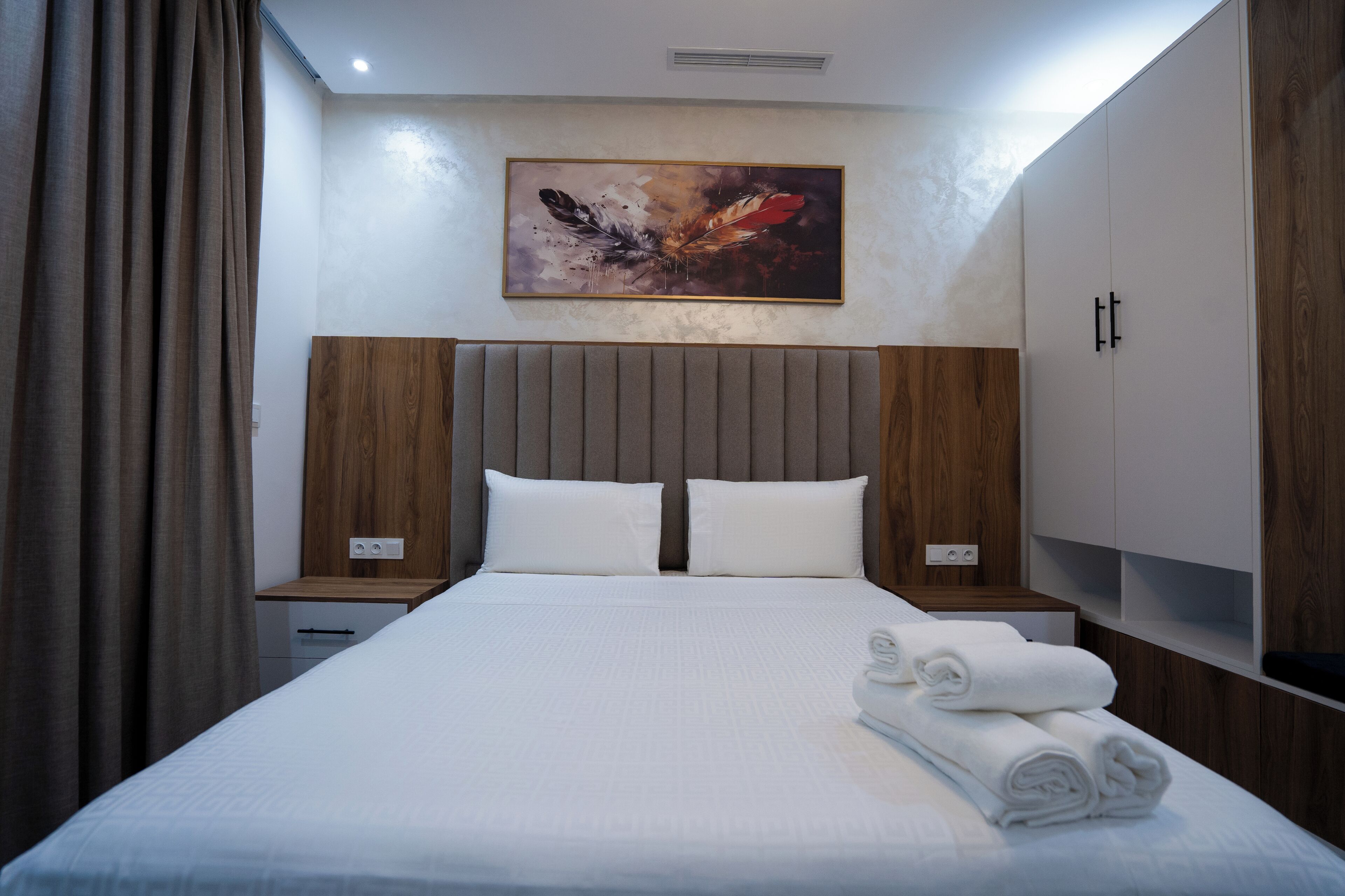 Une chambre d’hôtel avec un grand lit, une tête de lit en bois, du linge de lit blanc, un tableau au mur et une armoire en bois.