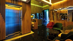 Un vestíbulo moderno con un mostrador de recepción de madera, una zona de estar con sillas coloridas y un ascensor grande.