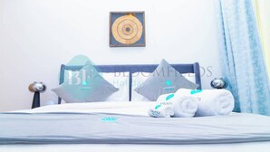 A neatly made bed with a pillow and a towel, a framed artwork on the wall, and a window with curtains.