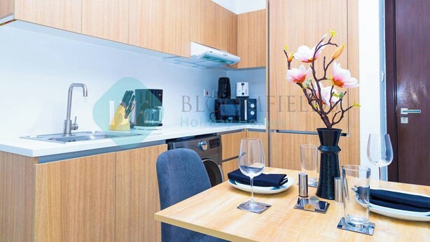 A modern kitchen with a built-in stove, a coffee maker, and a microwave. There is a dining table with a vase of flowers and a wine glass.