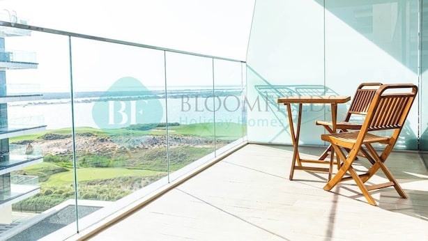 Un balcone con ringhiera in vetro, un tavolo e due sedie in legno.
