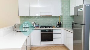 Una cucina moderna con mobili bianchi, un frigorifero in acciaio inossidabile, forno integrato e una parete di piastrelle verdi.