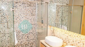 Un bagno moderno con cabina doccia in vetro, lavandino bianco e pannello di fondo in piastrelle.