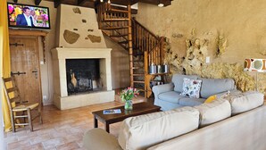 Una sala de estar acogedora con chimenea, un sofá, una escalera de madera y un televisor montado en la pared.