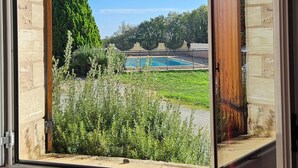 Una habitación con un ventanal que ofrece vistas a una piscina, zonas verdes y un muro de piedra.