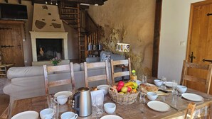 Un comedor rústico con una mesa de madera lista para el desayuno, una chimenea y una pared de piedra.