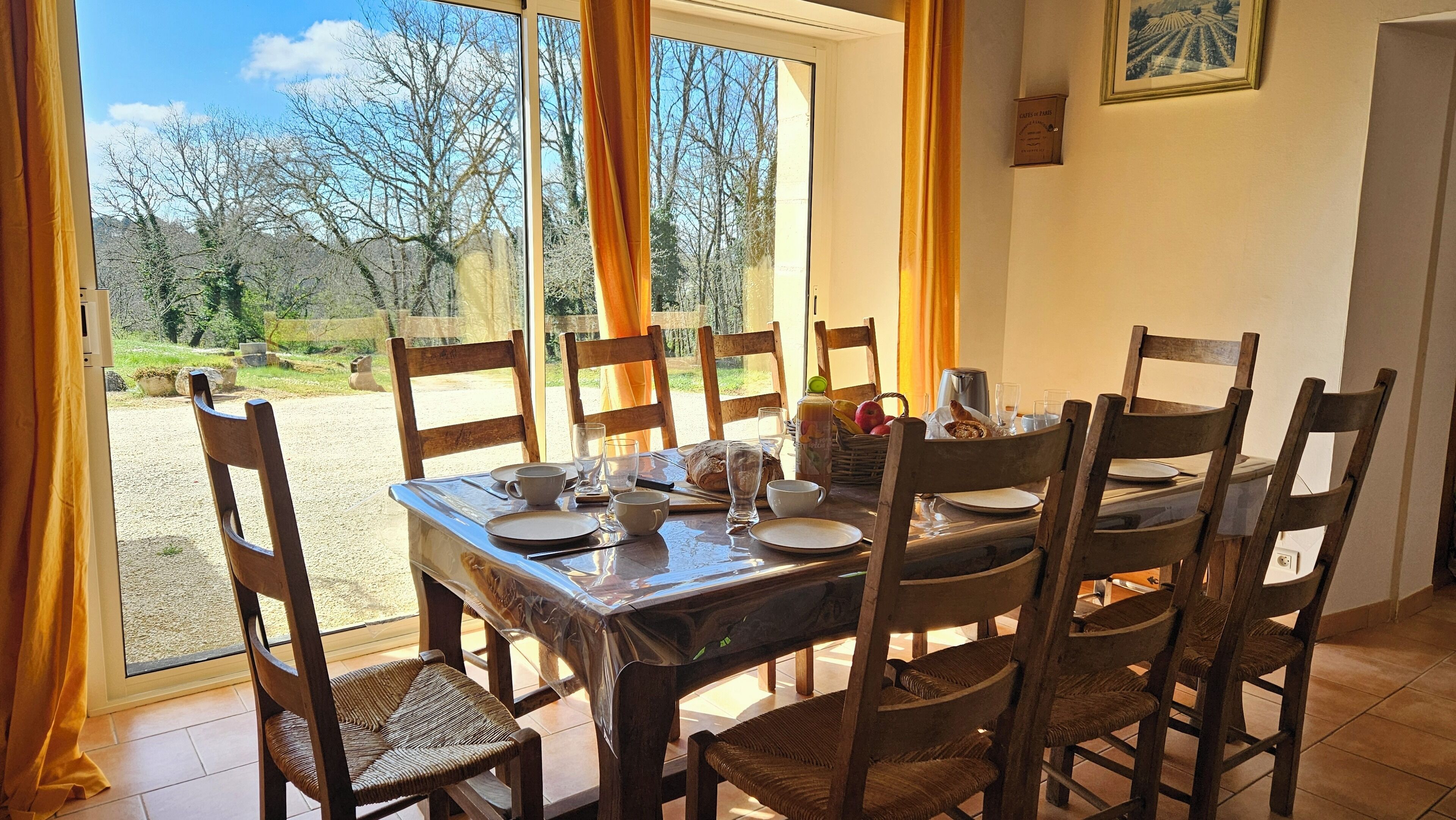 A dining table set for six with wooden chairs, a window with curtains, and a view of a garden.