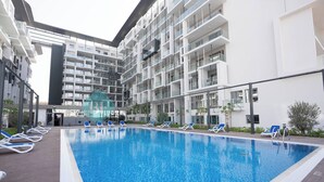 Een modern binnenzwembad met helderblauw water, omgeven door witte gebouwen met balkons en ligstoelen.