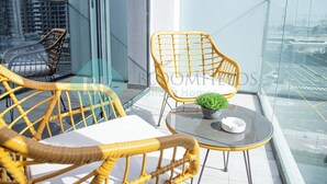 A balcony with wicker chairs and a small table, a potted plant, and a glass railing. - Bloomfields STU View Azizi Riviera Meydan (Dubai)