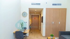 A modern hotel room with a wooden wardrobe, a dining area with a table and chairs, a sofa, and a small potted plant. - Bloomfields STU View Azizi Riviera Meydan (Dubai)