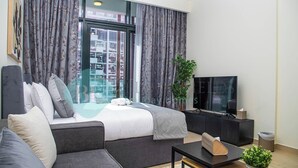 A modern hotel room with a large bed, grey sofa, a small table, a TV, and a potted plant. - Bloomfields STU View Azizi Riviera Meydan (Dubai)