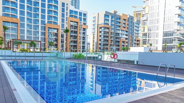 A rooftop swimming pool with clear blue water, surrounded by modern high-rise buildings and palm trees. - Bloomfields STU View Azizi Riviera Meydan (Dubai)