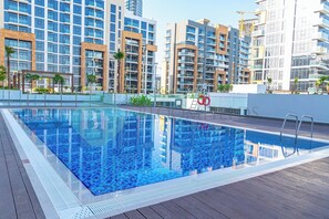 A rooftop swimming pool with clear blue water, surrounded by modern high-rise buildings and palm trees. - Bloomfields STU View Azizi Riviera Meydan (Dubai)