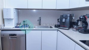 Una cucina moderna con mobili bianchi, una lavastoviglie in acciaio inossidabile, una macchina per il caffè e un lavandino.