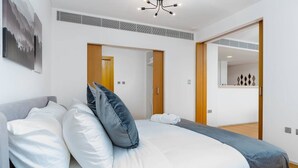 Et moderne hotelværelse med en stor seng, en grå sofa og en trædør, der fører til et badeværelse.