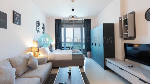 A modern hotel room with a bed, sofa, TV, and a view of the city. - Bloomfields Premium STU Canal View Julphar Tower (Abu Dabi)
